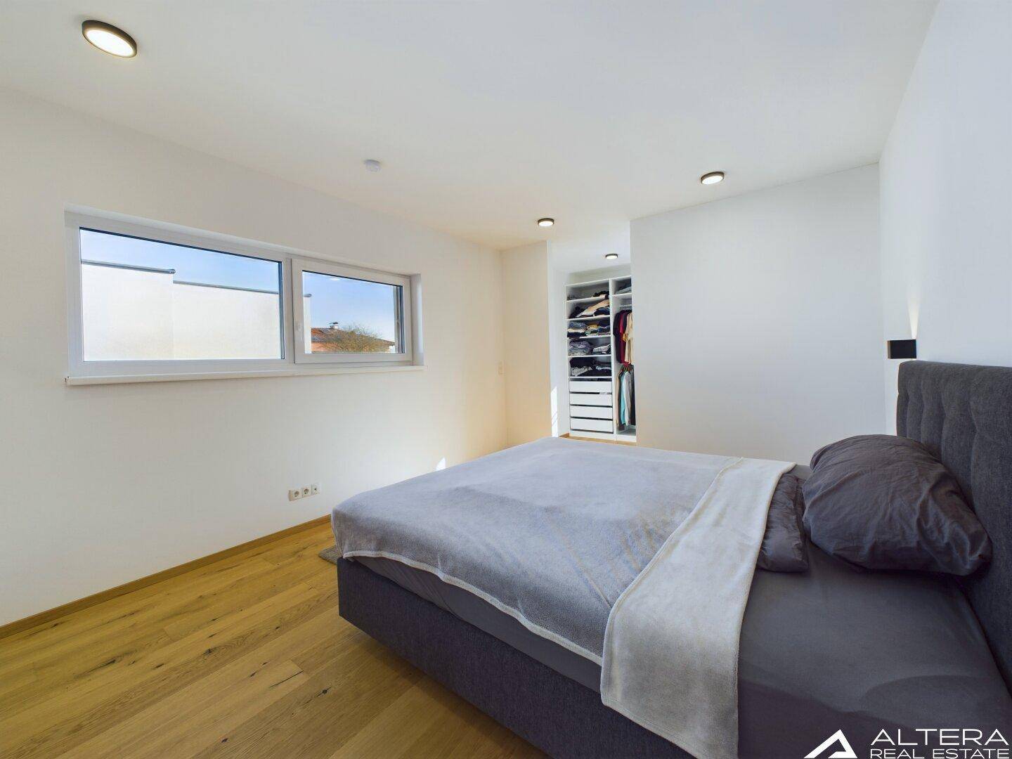 Schlafzimmer mit Doppelbett, Holzboden und offenem Zugang zu einem begehbaren Ankleidezimmer.