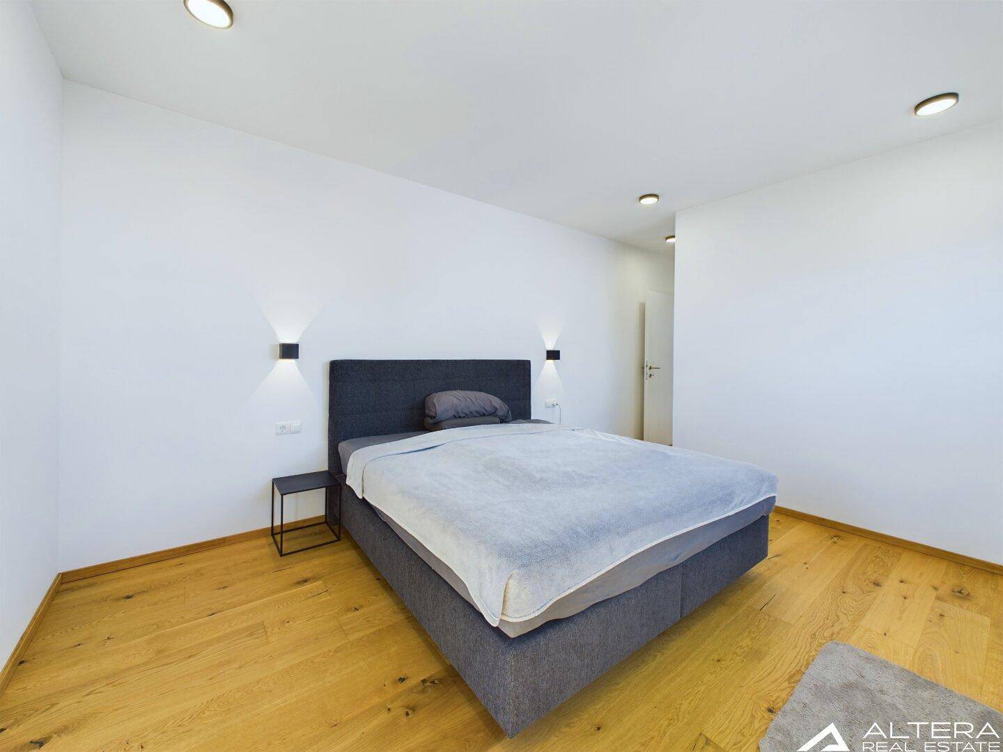 Helles Schlafzimmer mit Doppelbett, Holzboden und modernen Wandleuchten für angenehme Beleuchtung.