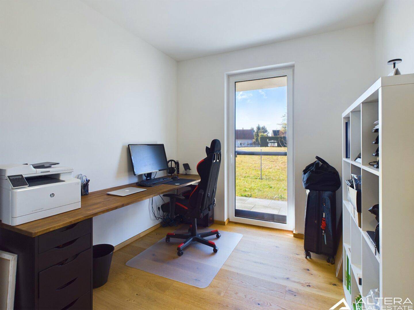 Helles Büro mit Holzboden, großem Schreibtisch und Zugang zu einem kleinen Außenbereich.