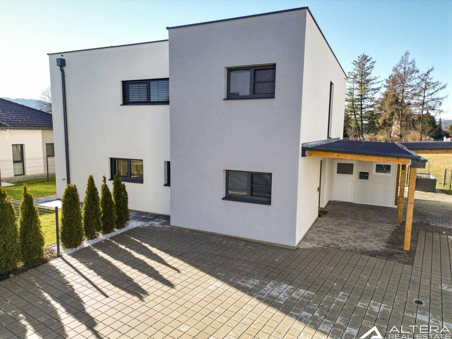 Vorderansicht eines modernen Hauses mit Carport und gepflasterter Einfahrt.