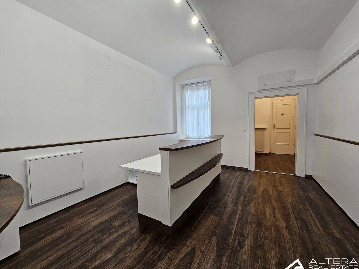 Empfangsbereich mit dunklem Boden, gewölbter Decke und einem Fenster, das Tageslicht hereinlässt.