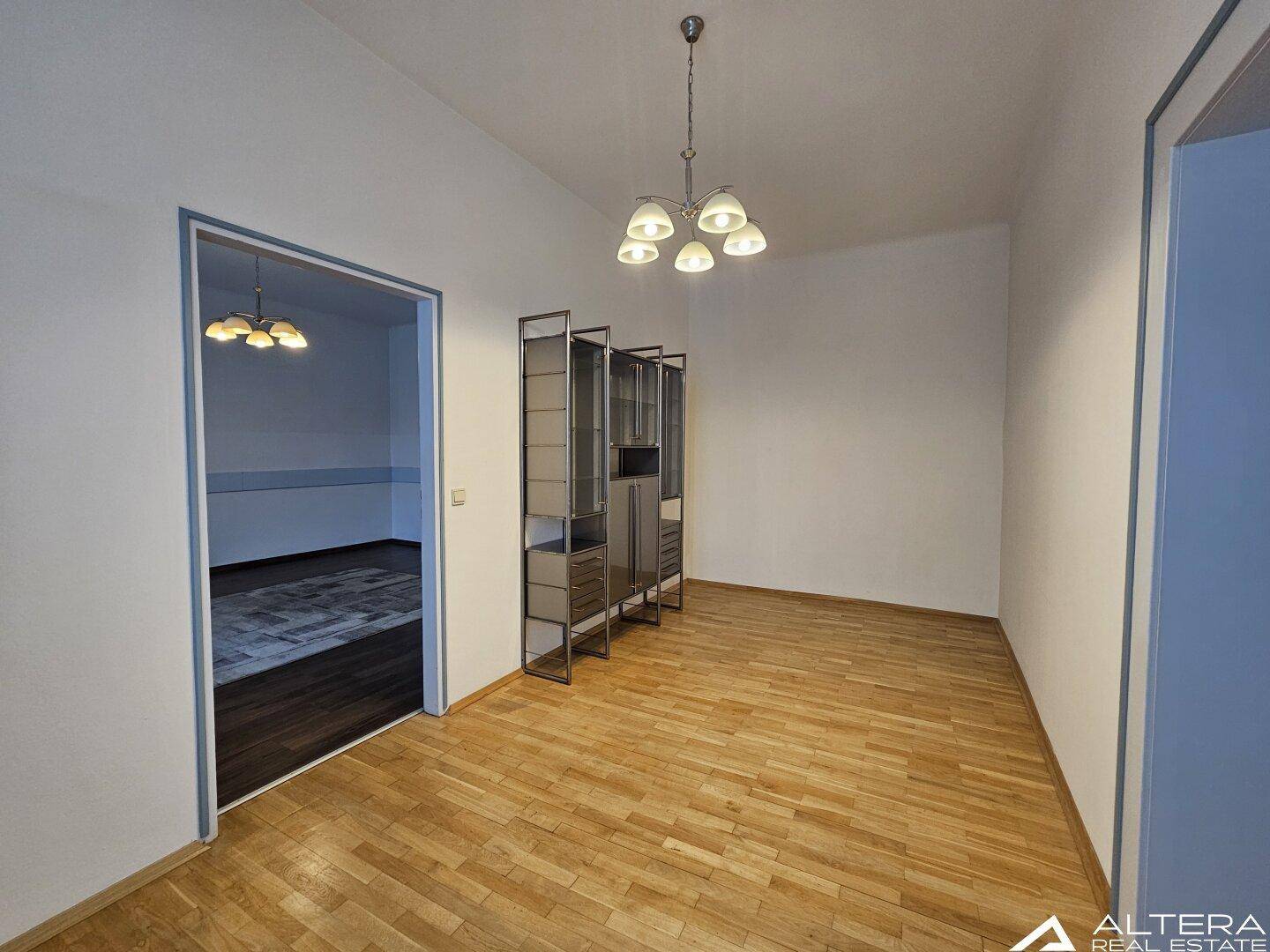 Heller Raum mit hellem Holzboden und einem modernen Regal, der zu einem weiteren Zimmer führt.