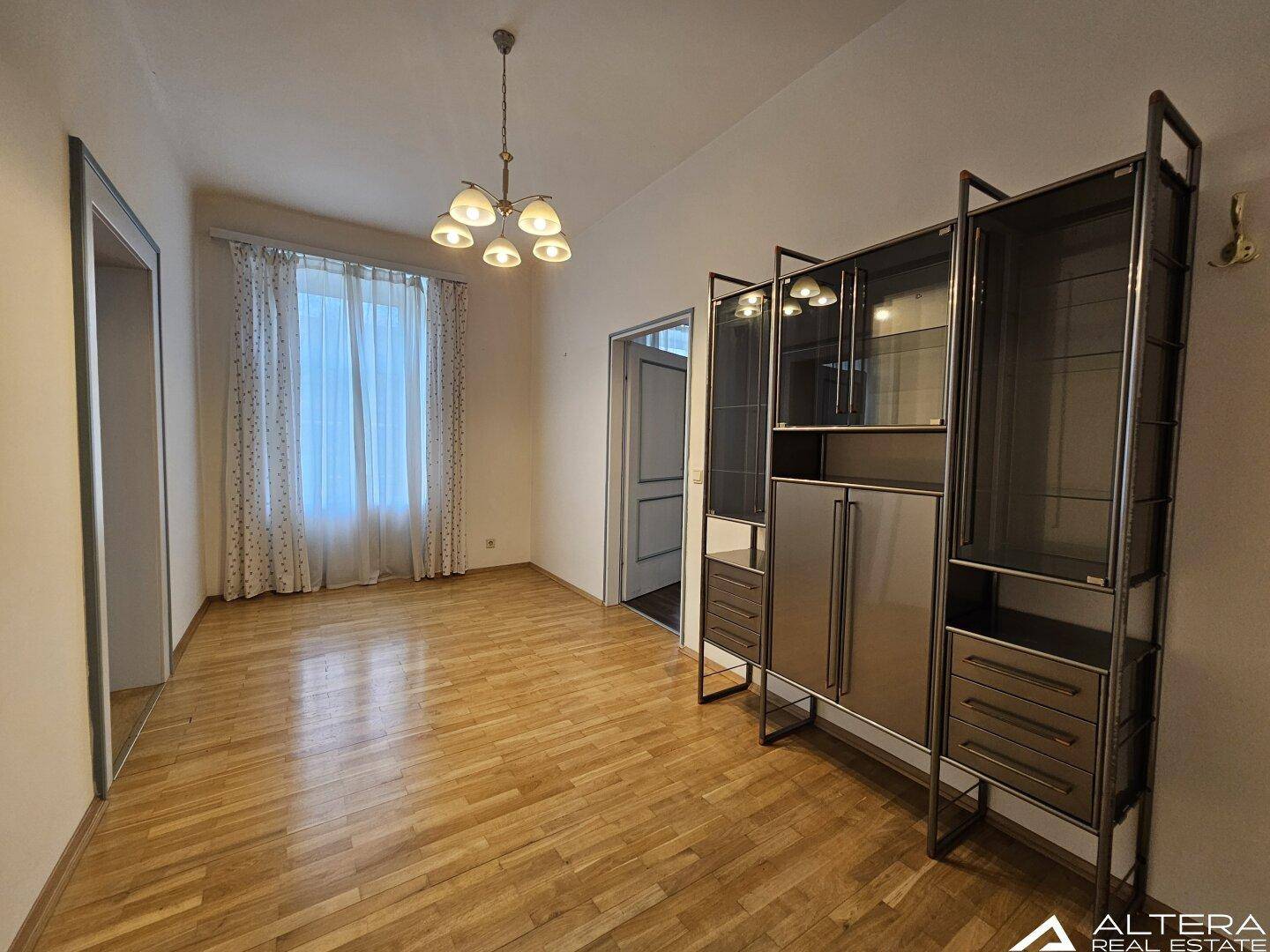 Geräumiger Raum mit hellem Holzboden, Fenster und einem eleganten Regal, das viel Stauraum bietet.