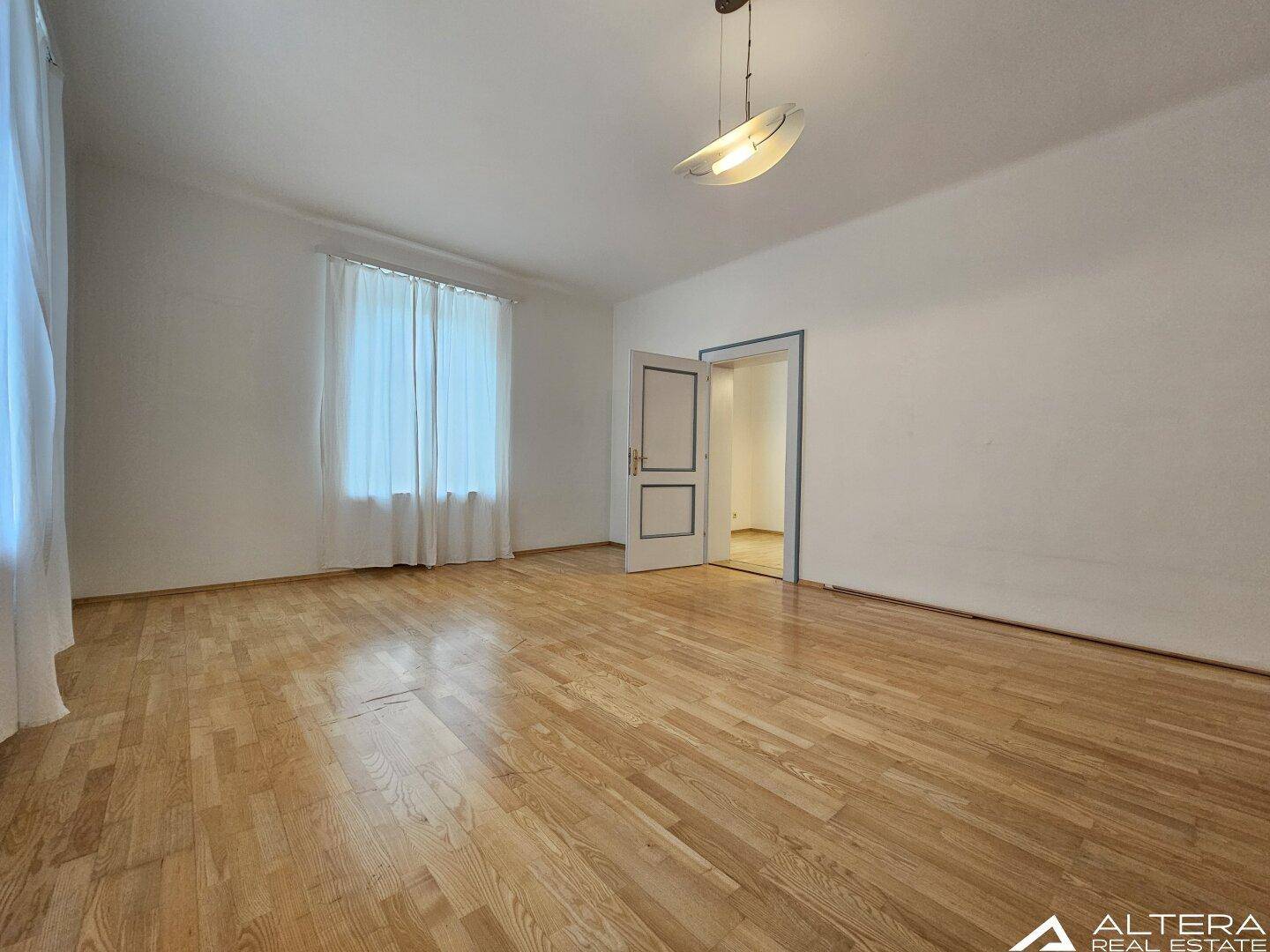 Heller Raum mit hellem Holzboden und einem großen Fenster, das den Raum mit Tageslicht füllt.