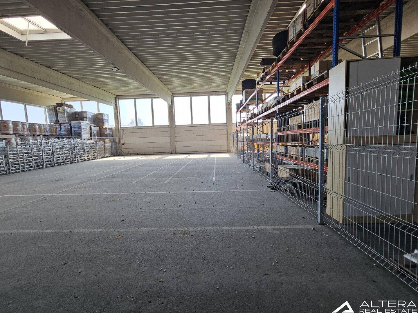 Geräumige Lagerhalle mit Betonboden, hohen Decken und großen Fenstern, die für eine helle Atmosphäre sorgen.