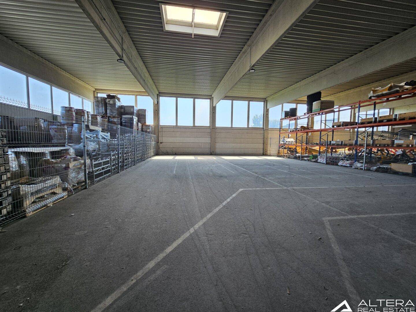 Helle Lagerhalle mit Betonboden, hohen Decken und Oberlichtern, die zusätzlich Tageslicht spenden.