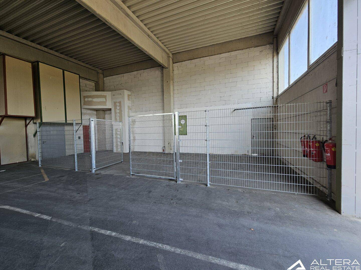 Geräumige Lagerhalle mit Betonboden, hohen Decken und Metallzäunen zur Abgrenzung von Lagerbereichen.