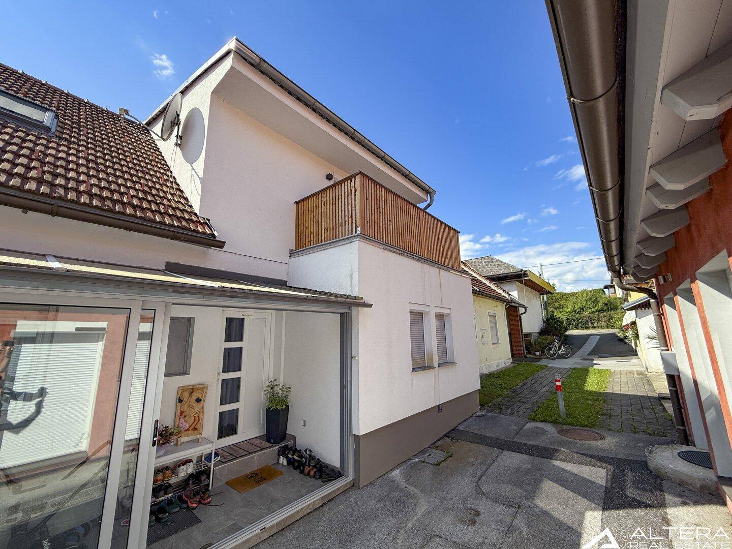 Seitenansicht des Hauses mit verglastem Eingangsbereich und einem Holzbalkon im Obergeschoss.