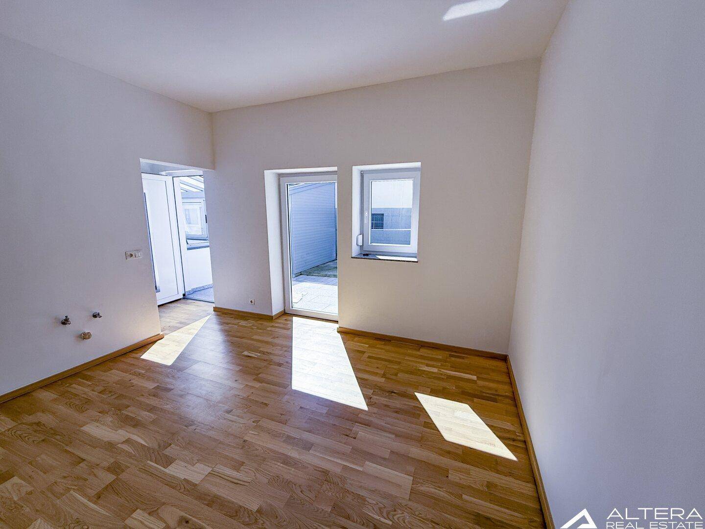 Lichtdurchfluteter Raum mit Holzboden und Zugang zu einem Außenbereich, ideal für Wohnzwecke.