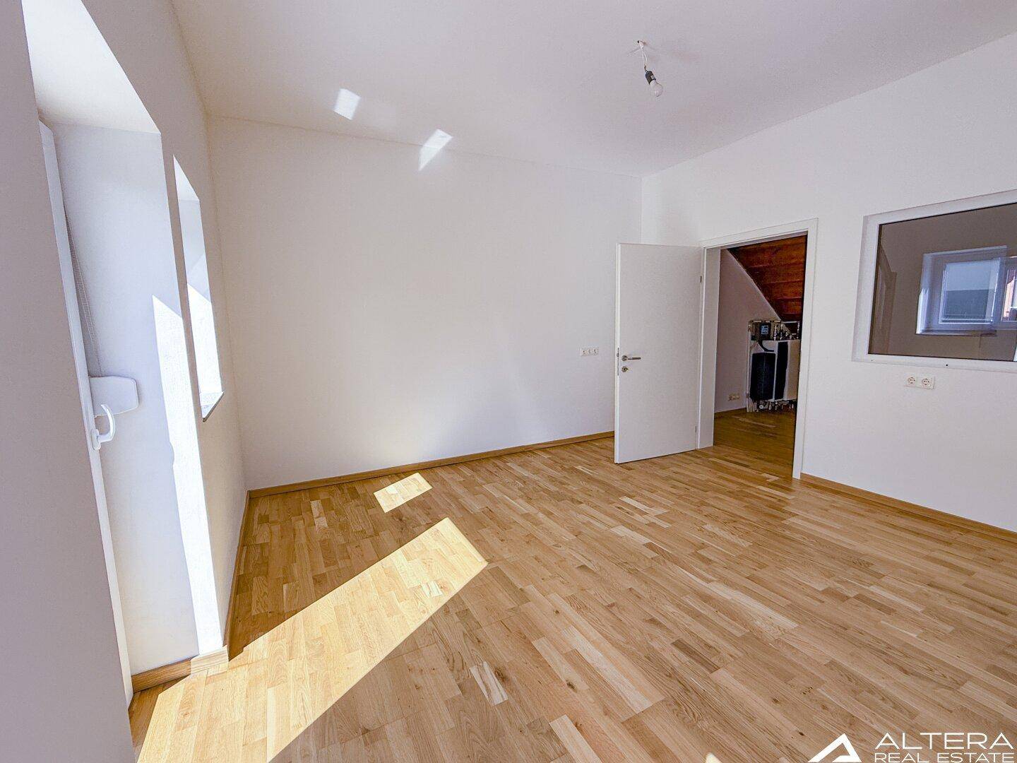 Geräumiger Raum mit Parkettboden und Zugang zu einem weiteren Zimmer, ideal für flexible Nutzung.