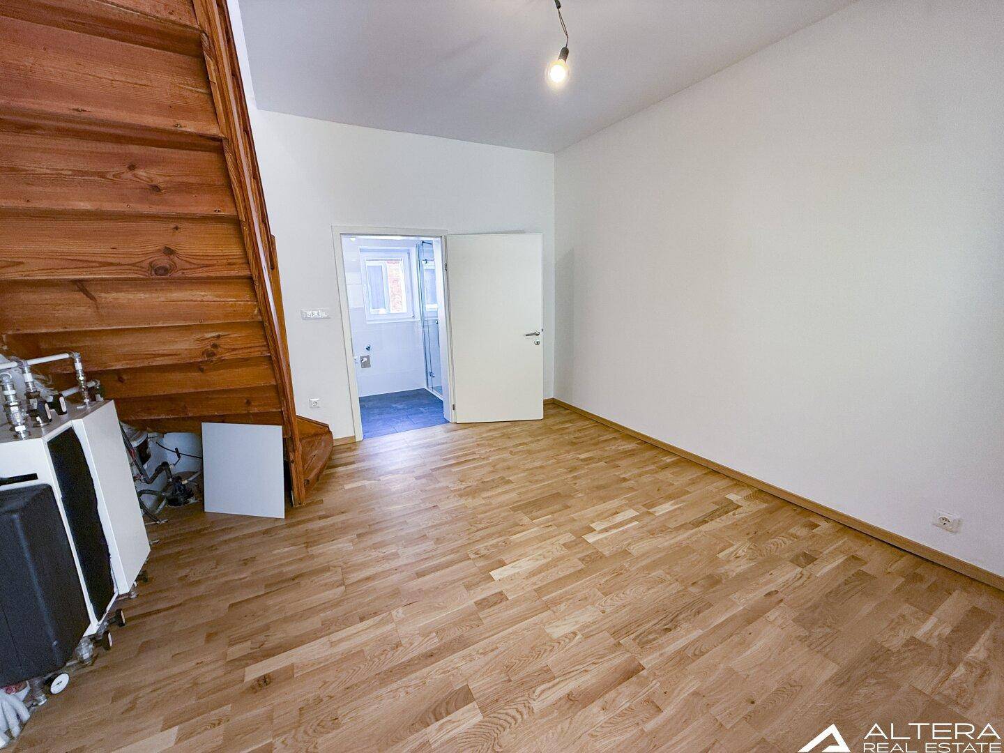 Heller Raum mit Holztreppe und Parkettboden, bietet Zugang zu einem angrenzenden Badezimmer.