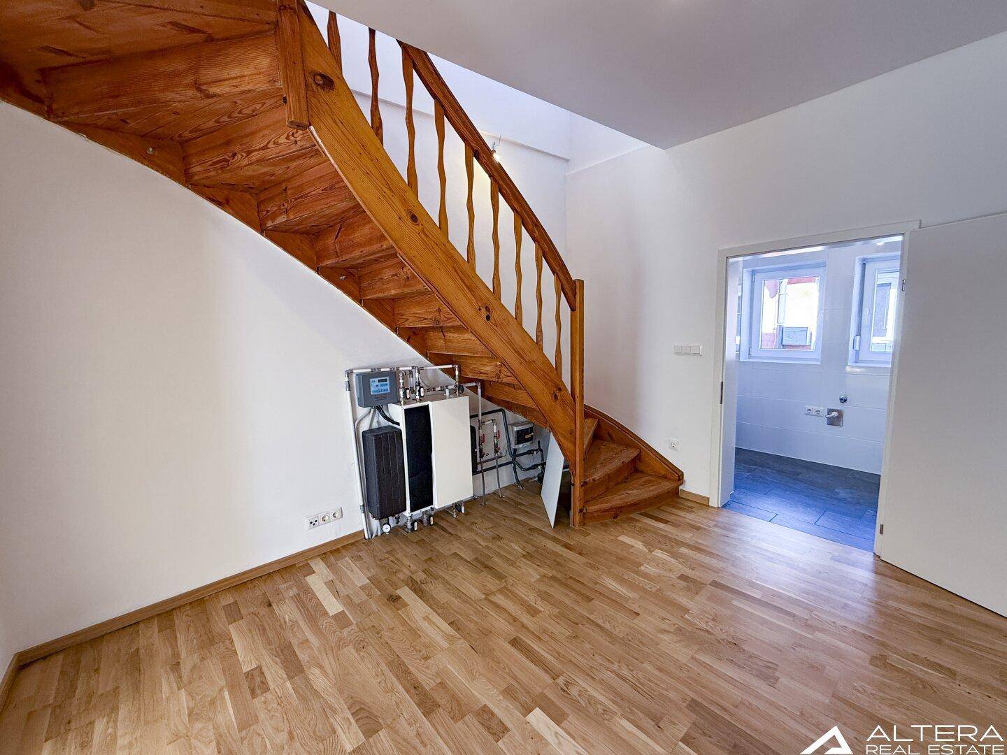 Geräumiger Raum mit markanter Holztreppe und Parkettboden, führt zu einem weiteren Bereich.