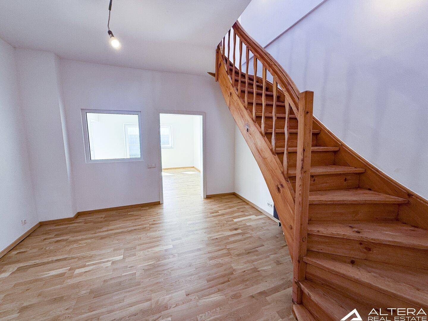 Heller Raum mit geschwungener Holztreppe und Parkettboden, verbindet verschiedene Wohnebenen.