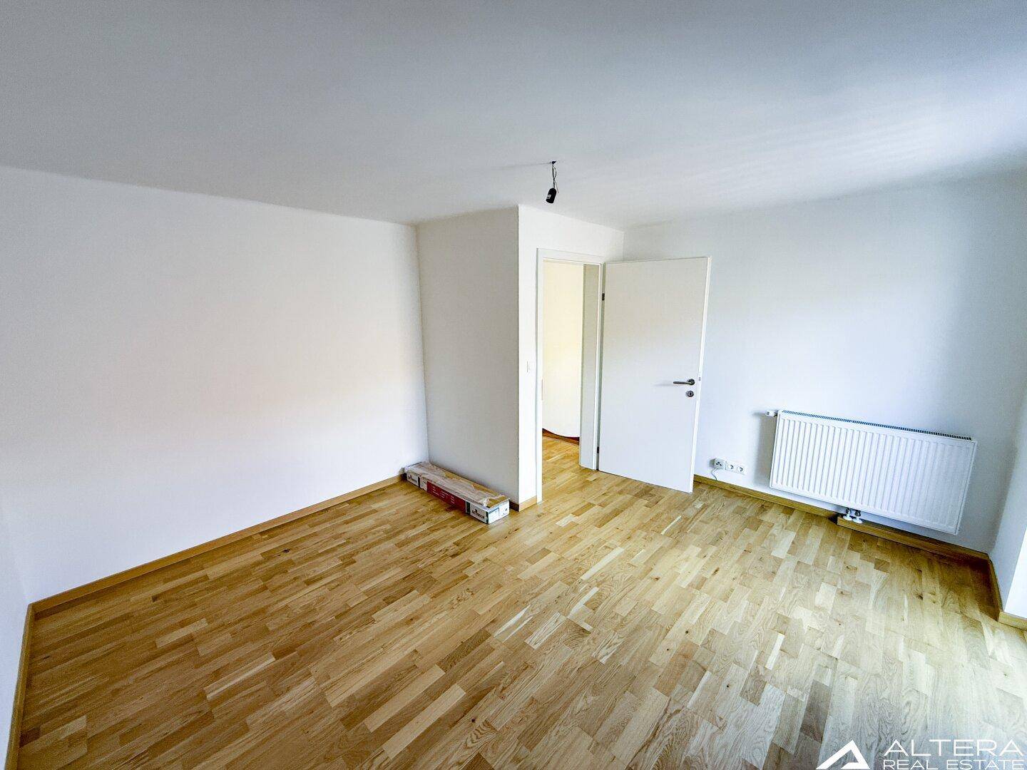 Helles Schlafzimmer mit Parkettboden und Heizkörper, bietet eine gemütliche Atmosphäre.
