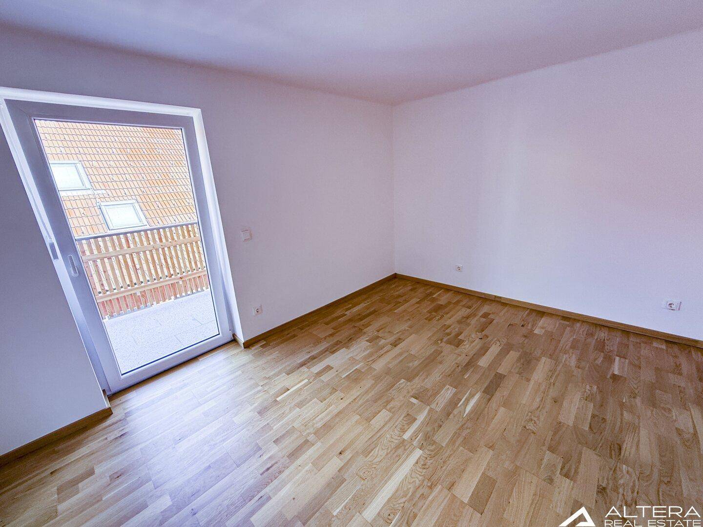 Helles Schlafzimmer mit Parkettboden und direktem Zugang zu einem Balkon, bietet viel Tageslicht.