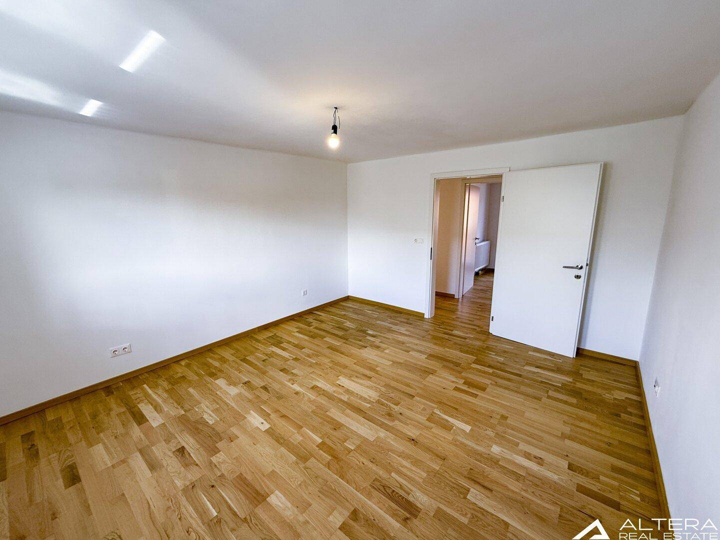 Helles Schlafzimmer mit Parkettboden und weiß gestrichenen Wänden, bereit zur individuellen Gestaltung.