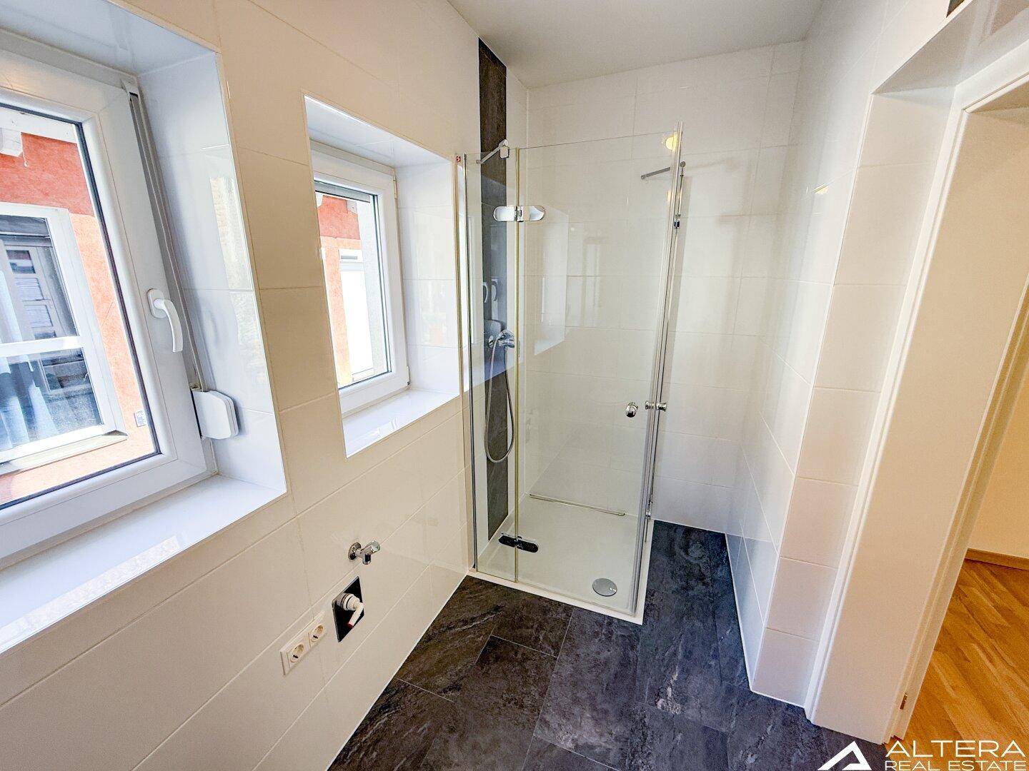 Modernes Badezimmer mit begehbarer Dusche, dunklen Bodenfliesen und weißen Wandfliesen.
