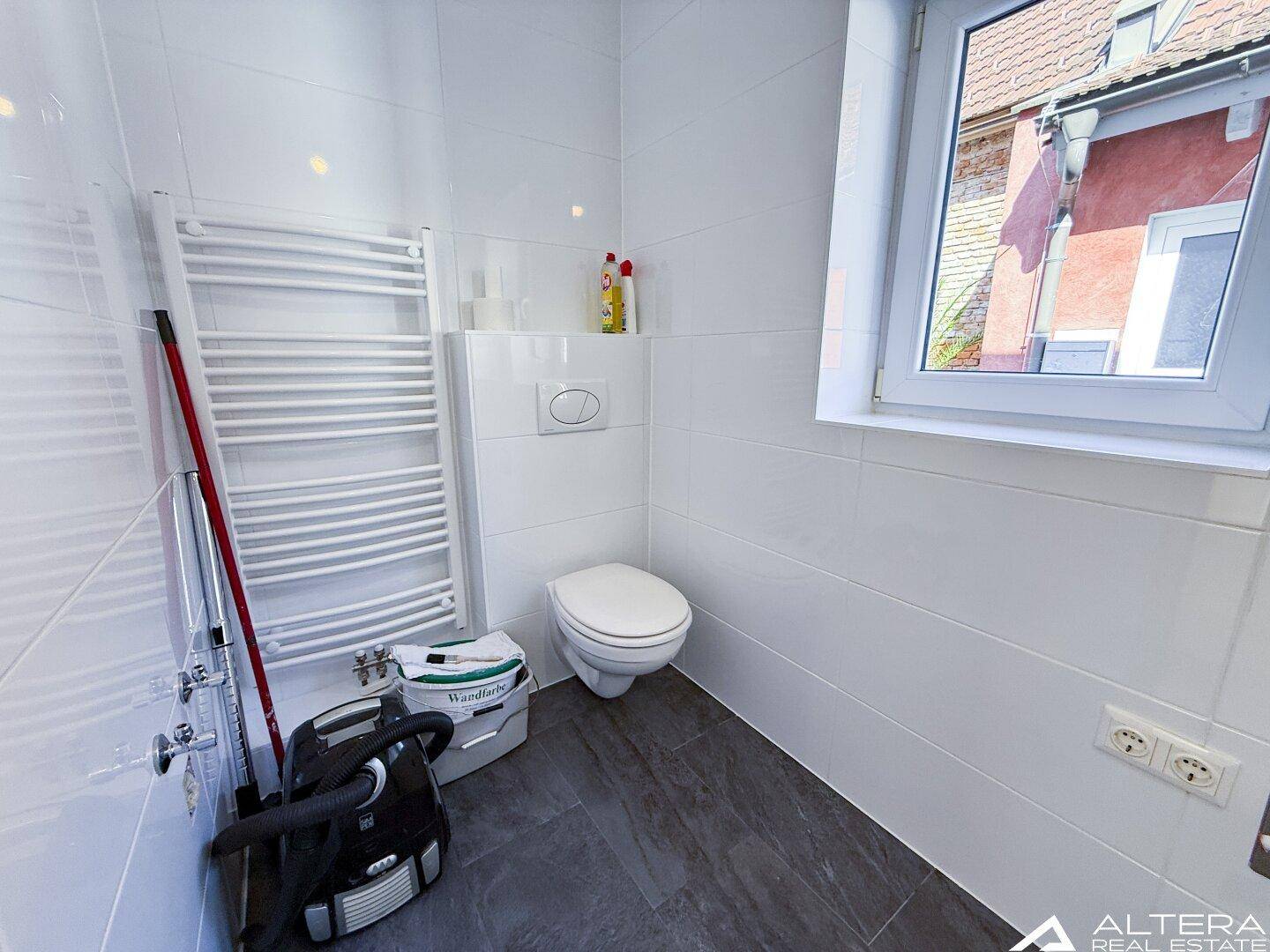 Helles Badezimmer mit wandhängendem WC, beheiztem Handtuchhalter und Fenster.