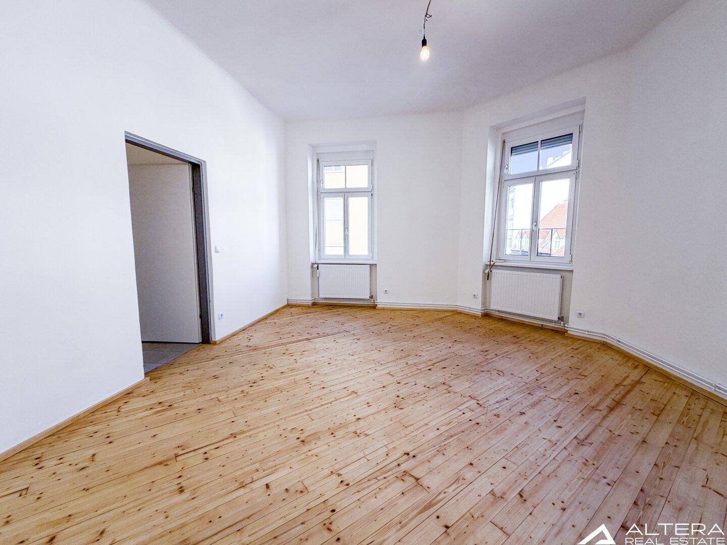 Großes, helles Zimmer mit Holzdielenboden und zwei Fenstern, bietet vielseitige Nutzungsmöglichkeiten.