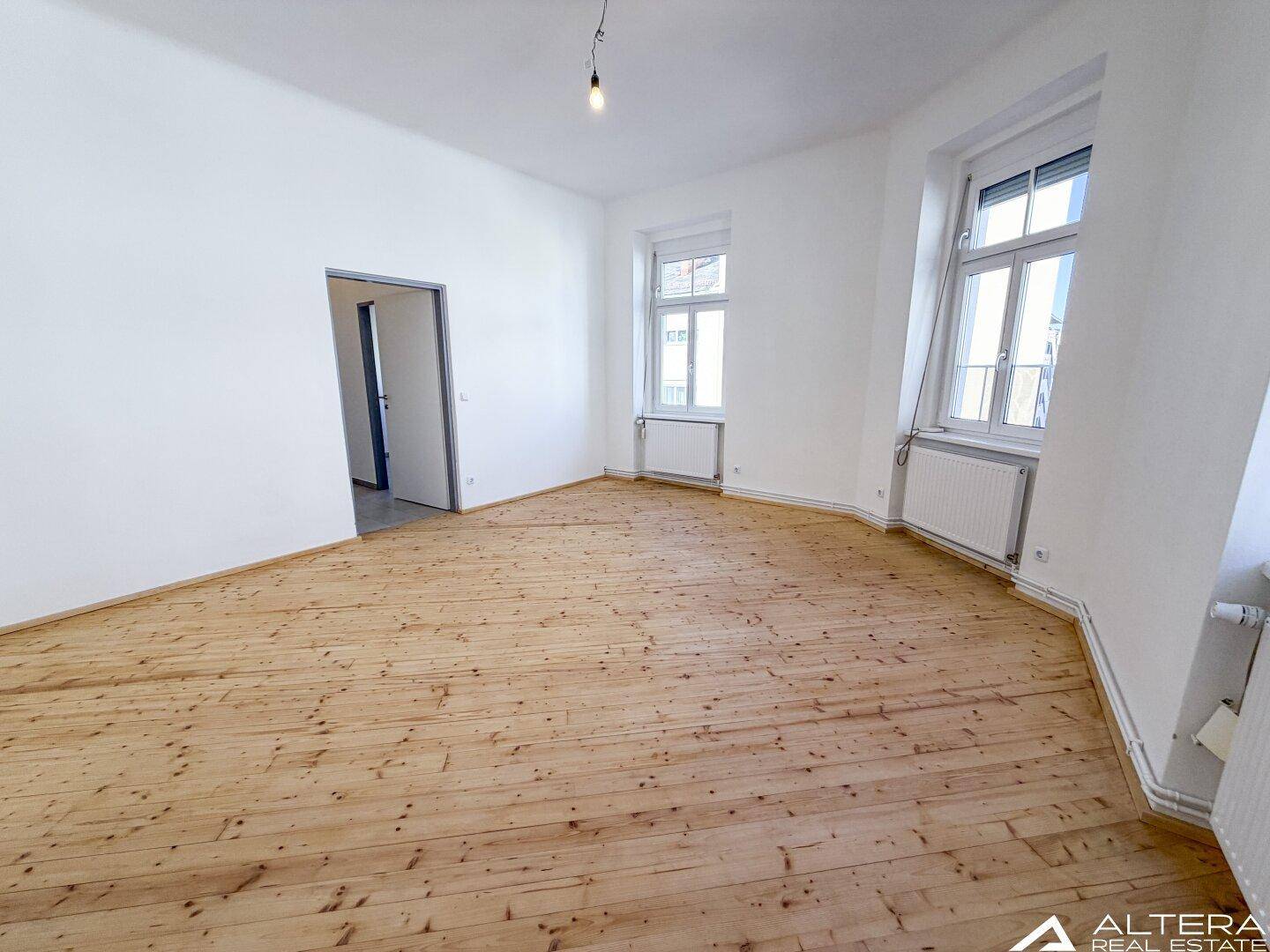 Geräumiges, helles Zimmer mit Holzdielenboden und Zugang zu einem weiteren Bereich.