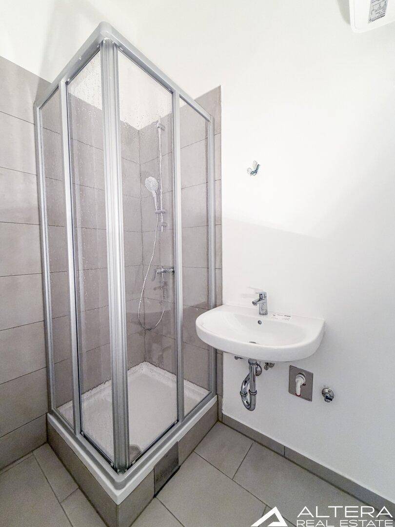 Modernes Badezimmer mit Duschkabine und Waschbecken, ausgestattet mit grauen Fliesen.