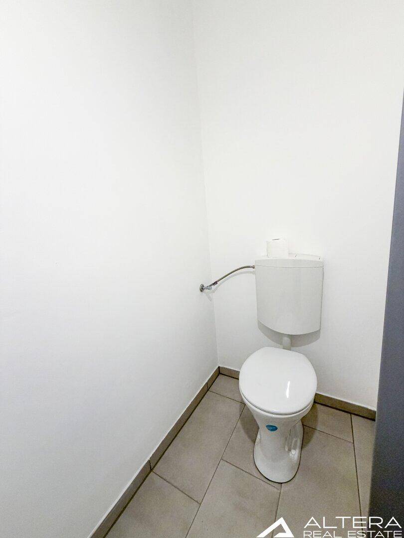 Separates WC mit Toilette und grauen Fliesen, sauber und funktional gestaltet.