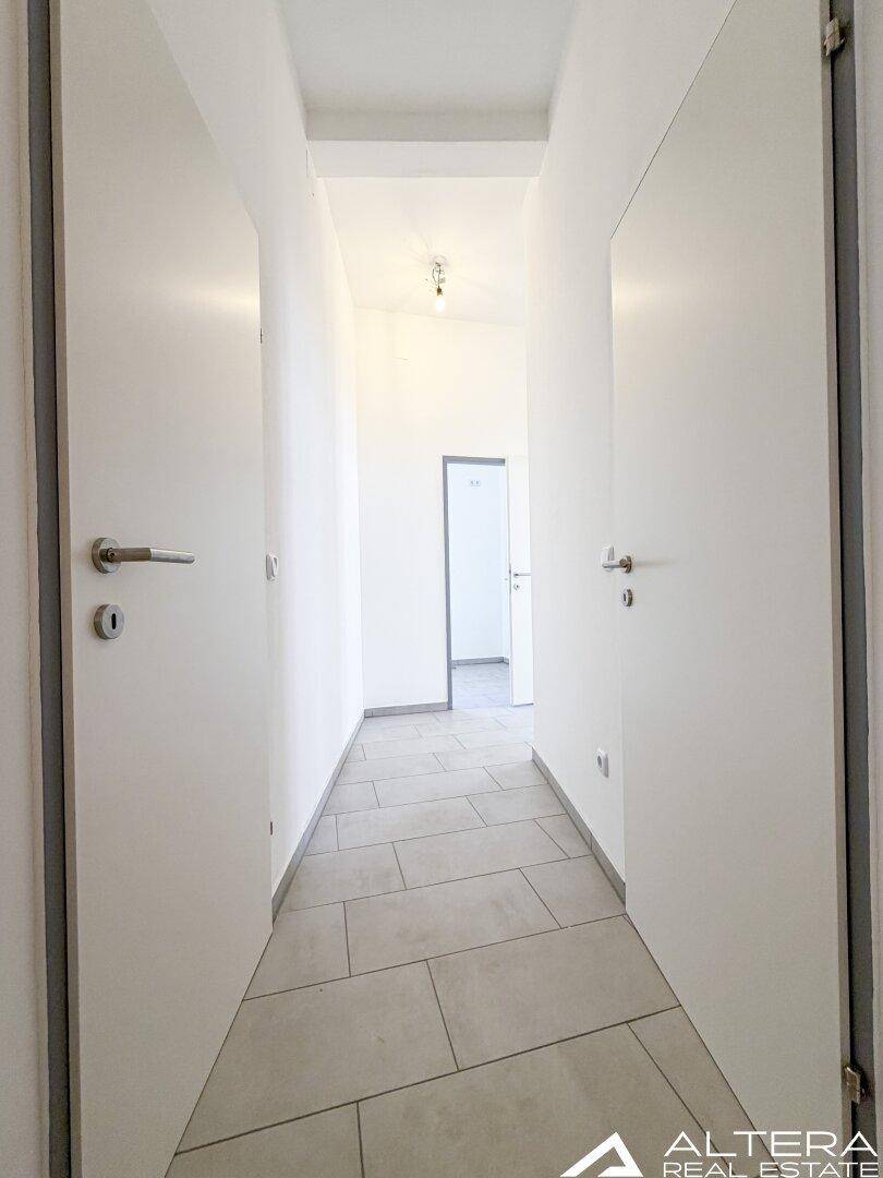 Langer, heller Flur mit grauen Fliesenboden, der einen Blick in die angrenzenden Räume ermöglicht.