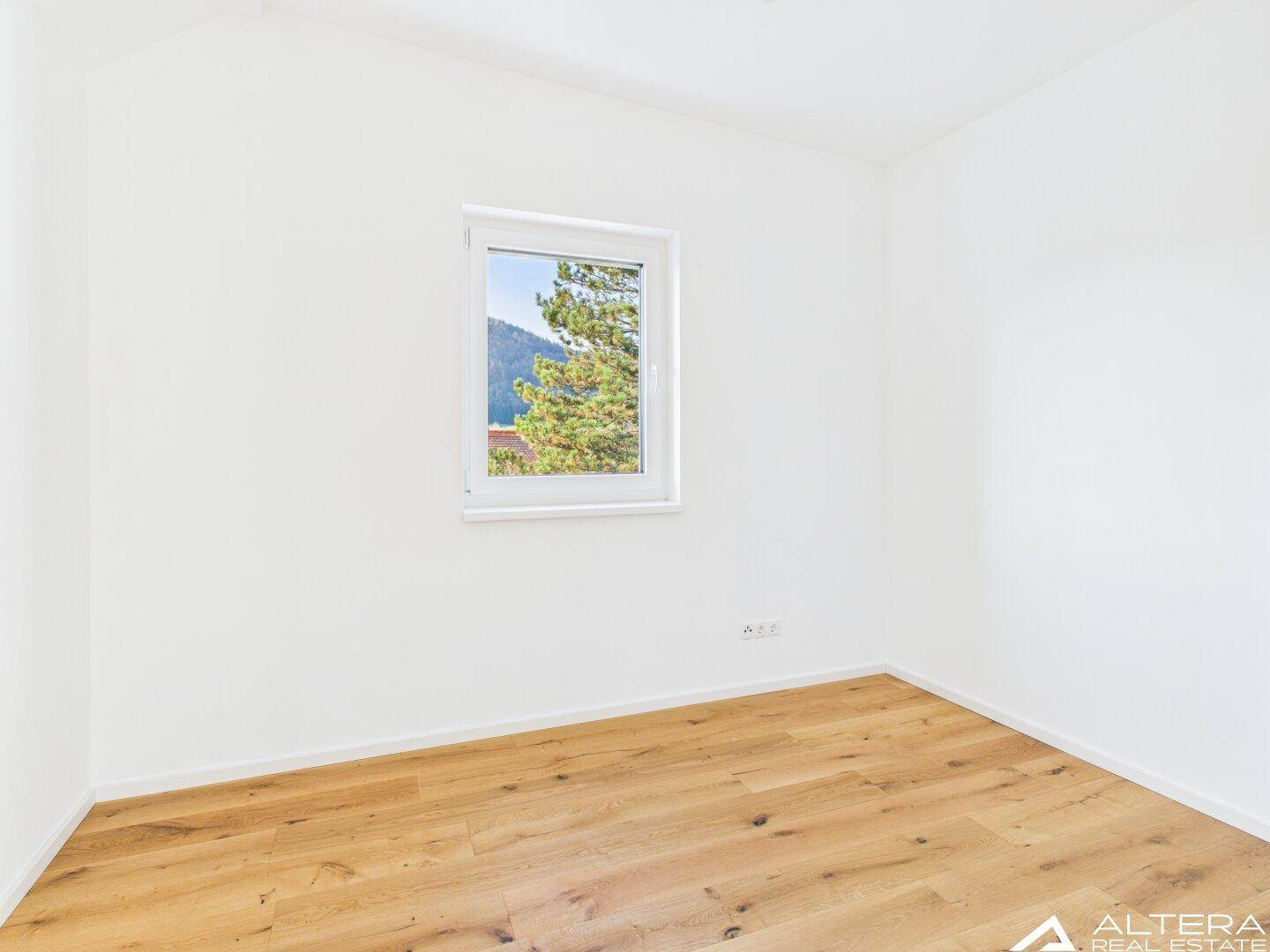 Ruhiges Zimmer mit Holzboden und einem Fenster mit Blick auf Bäume und Berge.