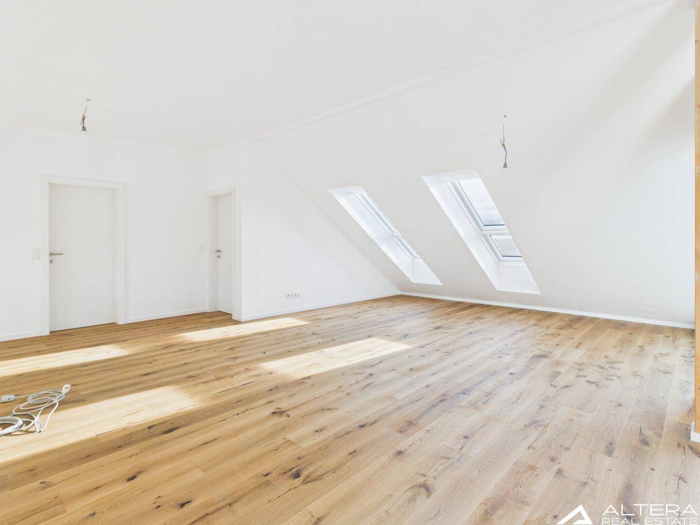 Geräumiger, heller Raum mit Holzboden, Dachschrägen und zwei Dachfenstern, bereit zum Einrichten.