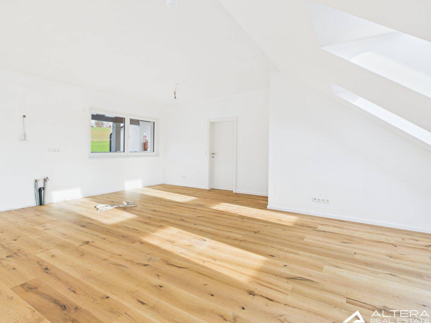 Helles Zimmer mit Holzboden, weiß gestrichenen Wänden und einem Dachfenster für viel Tageslicht.