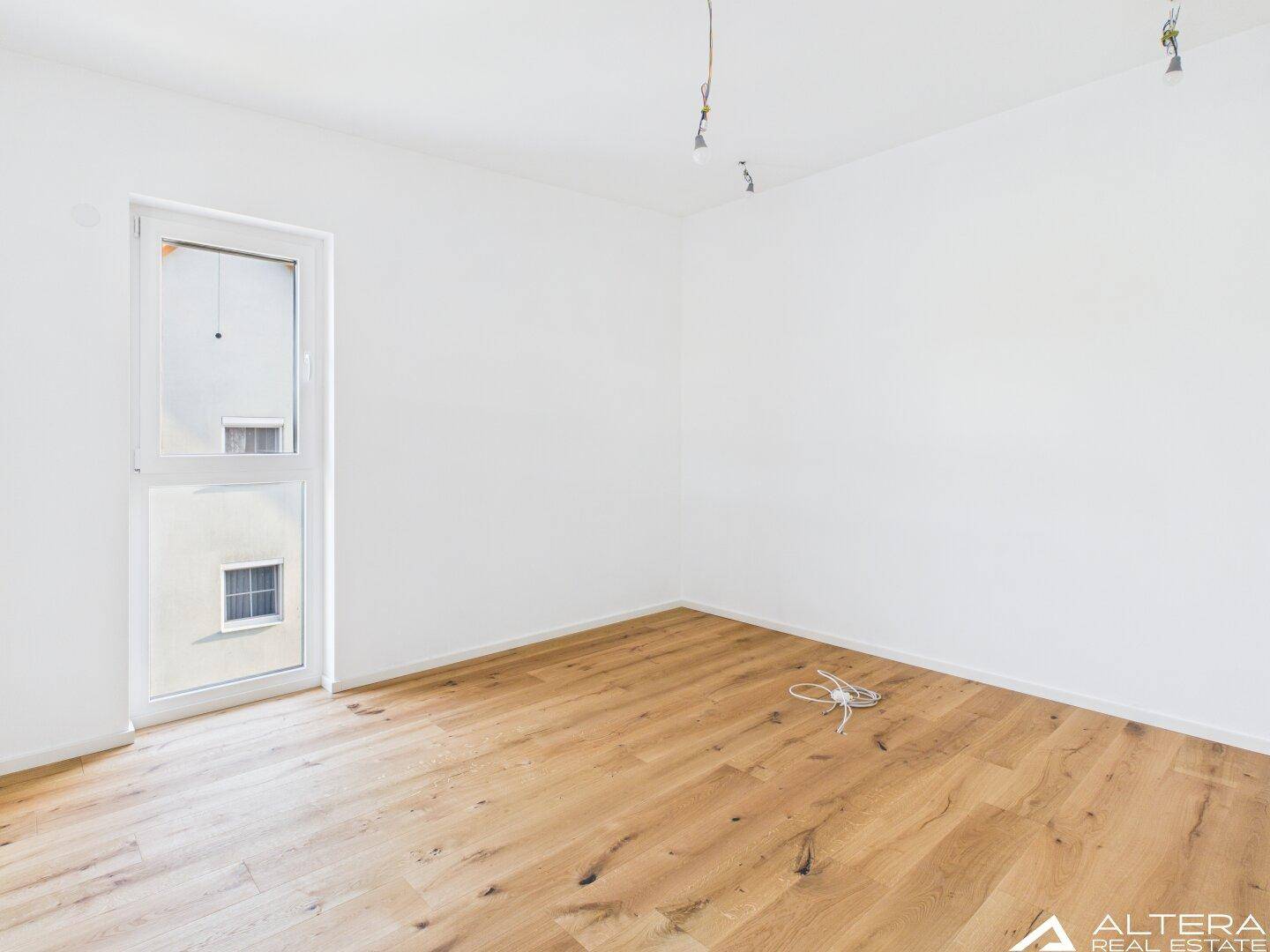 Freundliches Zimmer mit Holzboden und bodentiefem Fenster, das viel Licht spendet.