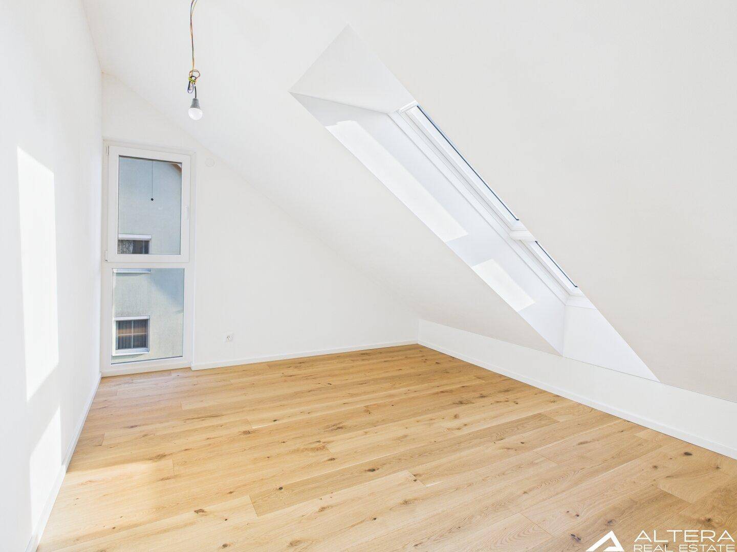 Helles Zimmer mit Holzboden, Dachschräge und großem Dachfenster sowie bodentiefem Fenster.