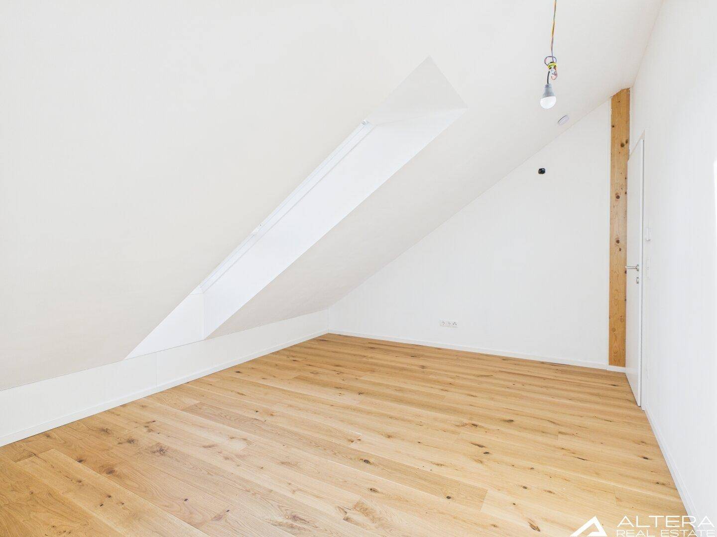 Ruhiges Zimmer mit Holzboden, Dachschräge und großem Dachfenster, ideal als Schlafzimmer.
