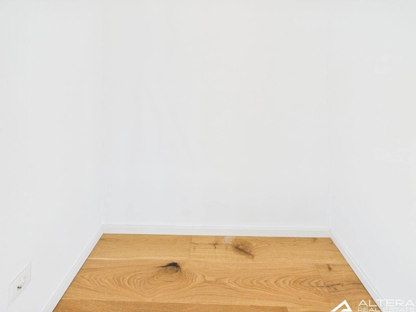Detailaufnahme des neuen Holzbodenbelags und der weißen Wand in einem hellen Raum.