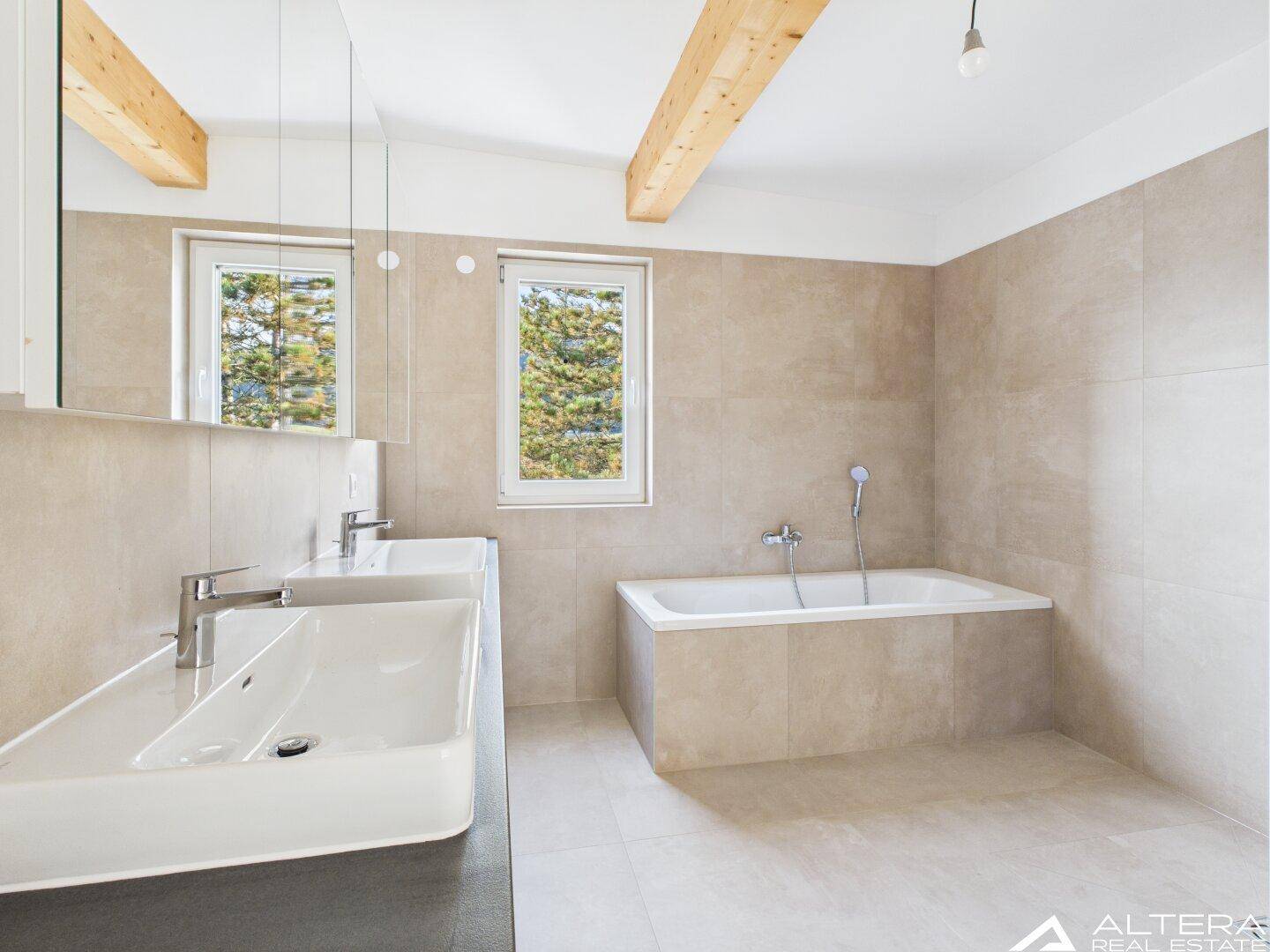 Modernes Badezimmer mit beigefarbenen Fliesen, Doppelwaschbecken, Badewanne und Holzbalken.