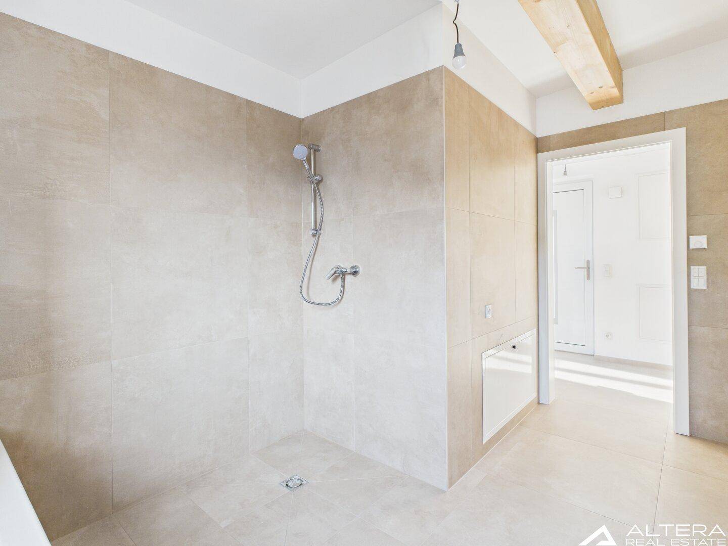 Geräumige Dusche im modernen Badezimmer mit beigefarbenen Fliesen und Holzbalken.