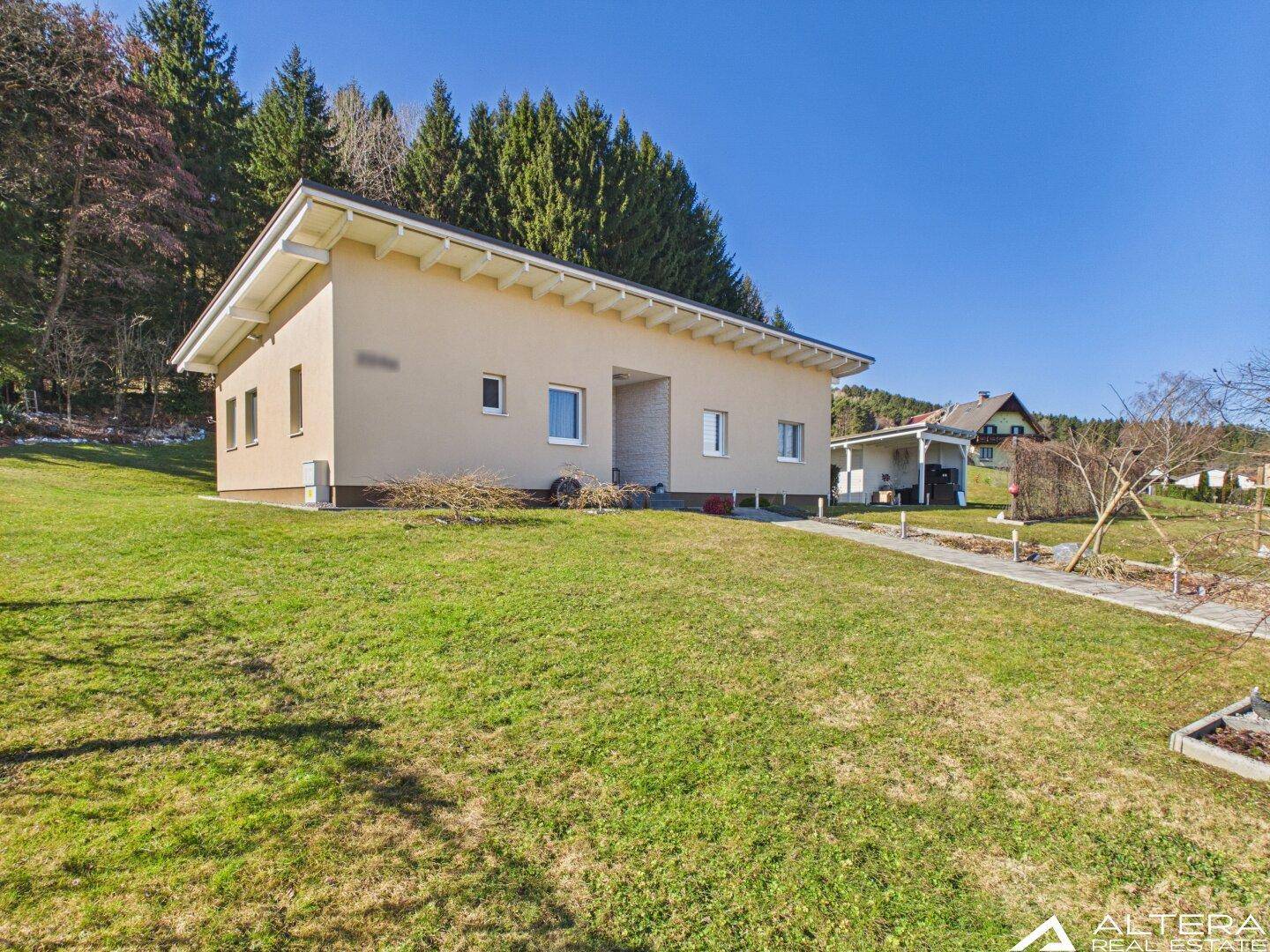 Seitenansicht des modernen Einfamilienhauses mit gepflegtem Rasen und Wald im Hintergrund.