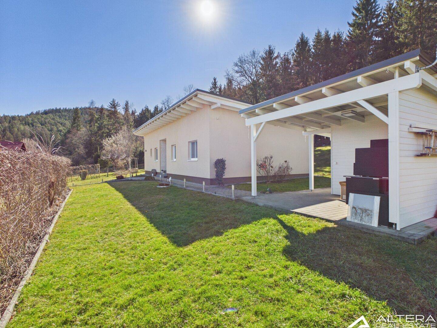 Ansicht des Hauses mit Carport und weitläufigem Garten unter blauem Himmel.