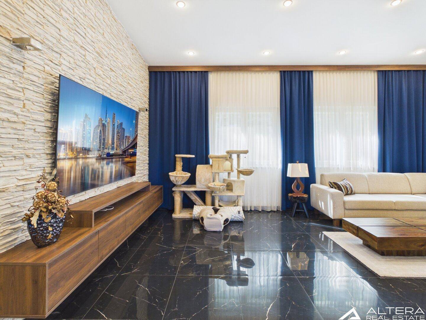 Wohnzimmer mit großem Fernseher, Steinwand und dunklem Fliesenboden.