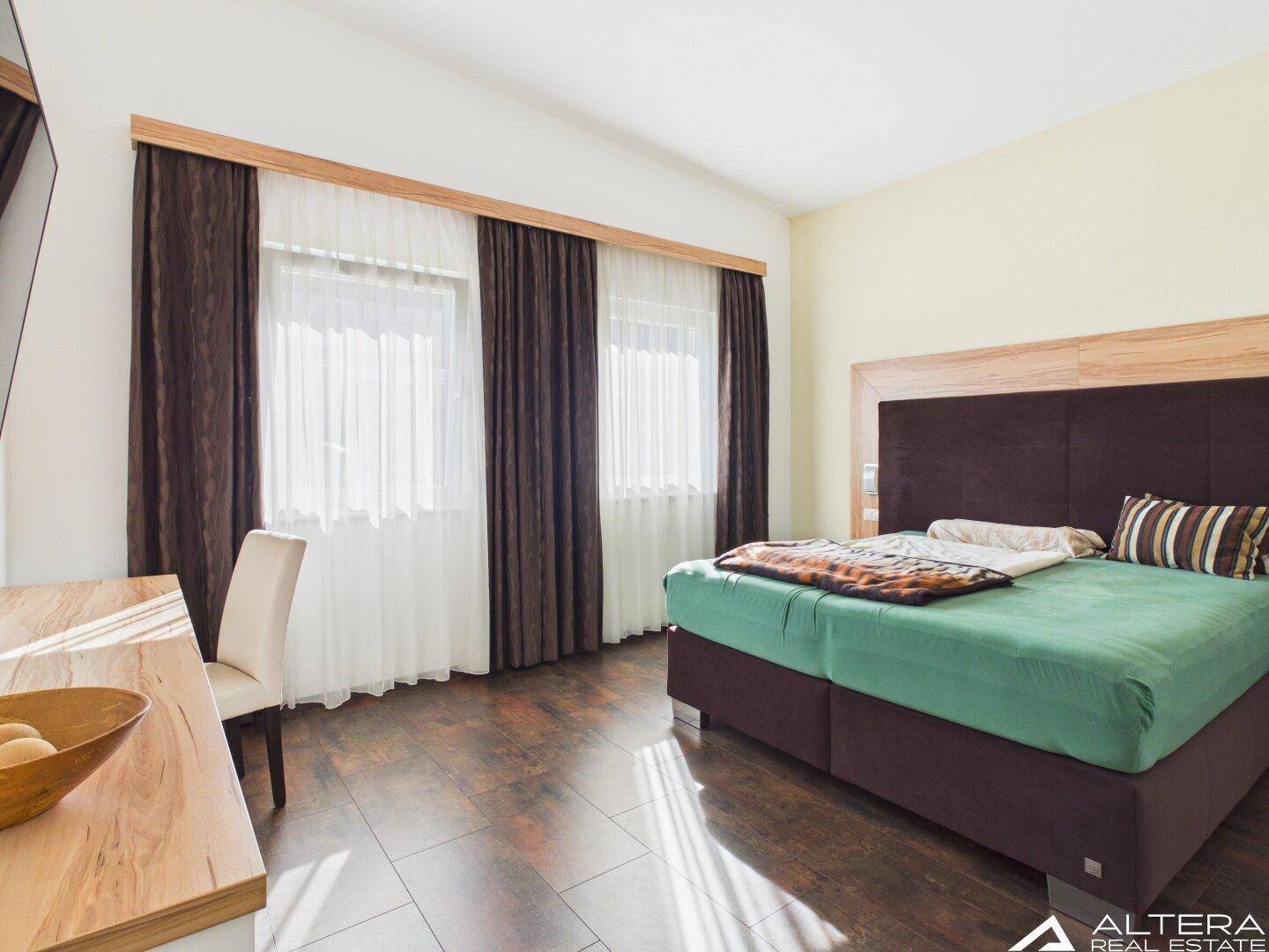 Schlafzimmer mit Doppelbett, Holzboden und großen Fenstern für viel Tageslicht.