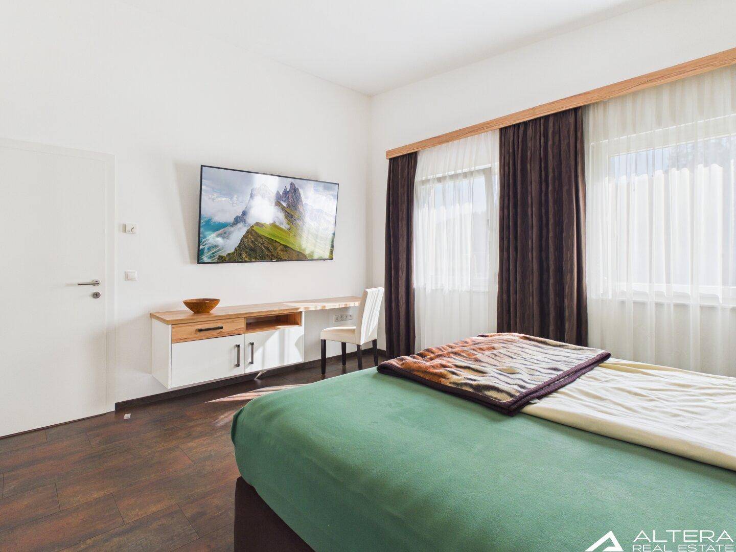 Helles Schlafzimmer mit Wandfernseher, Schreibtisch und Blick nach draußen.