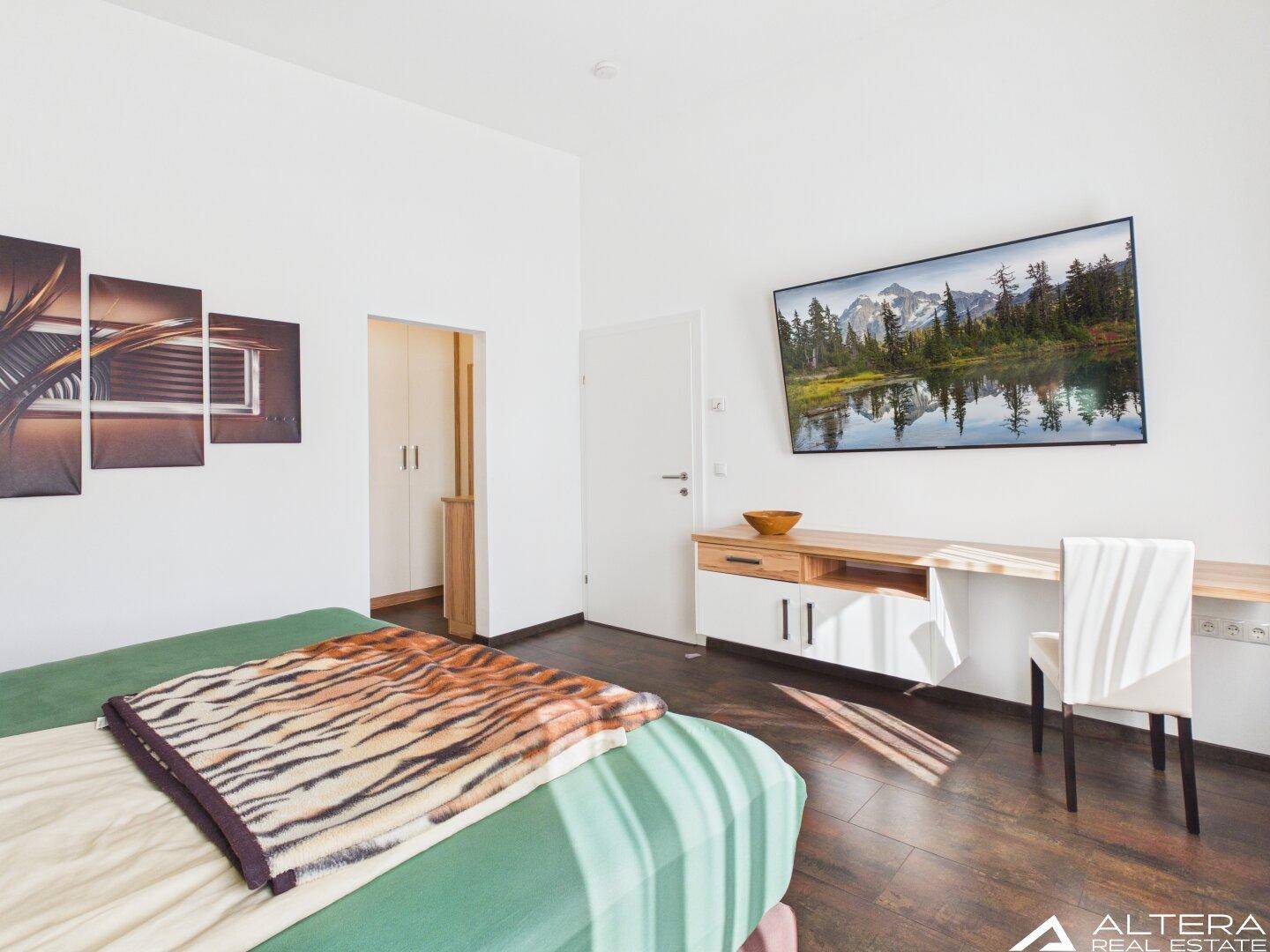 Schlafzimmer mit modernem Dekor, Holzboden und Zugang zu einem weiteren Raum.