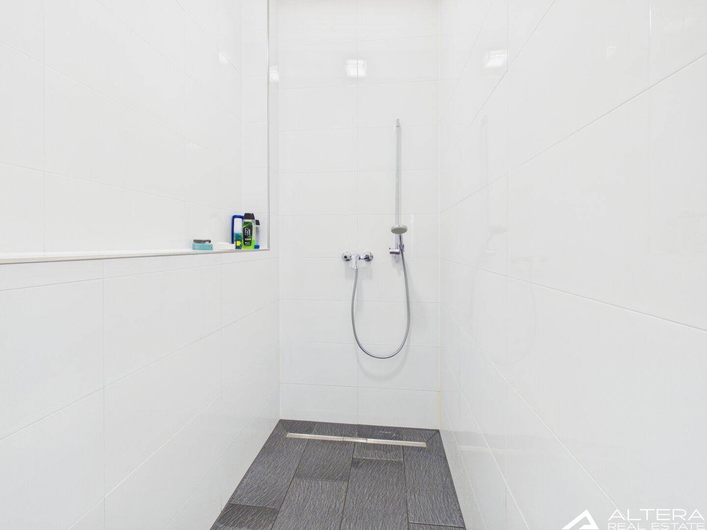 Moderne begehbare Dusche mit dunklem Fliesenboden und weißen Wänden.