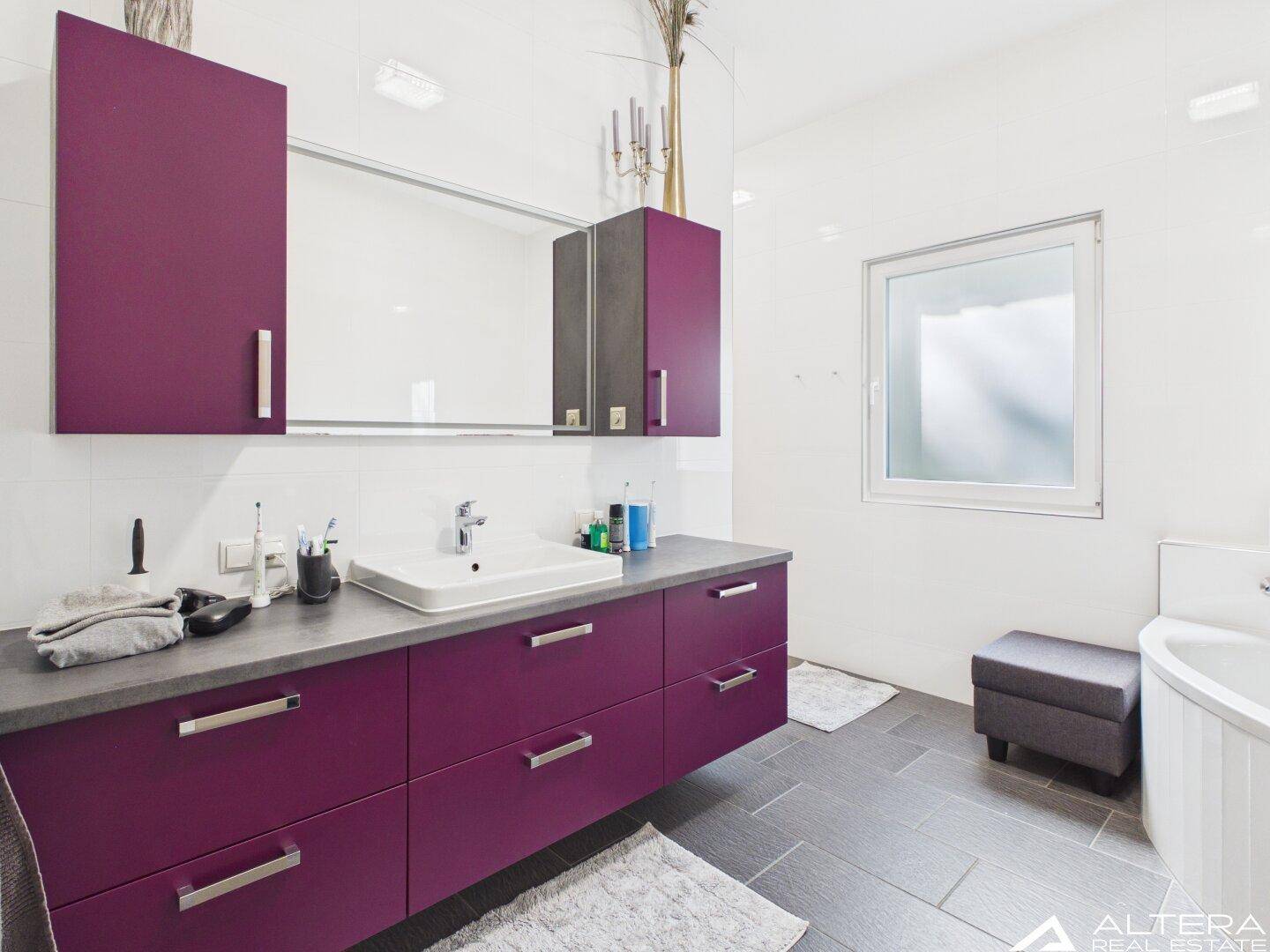 Modernes Badezimmer mit lila Waschtischunterschrank, Badewanne und Fenster.