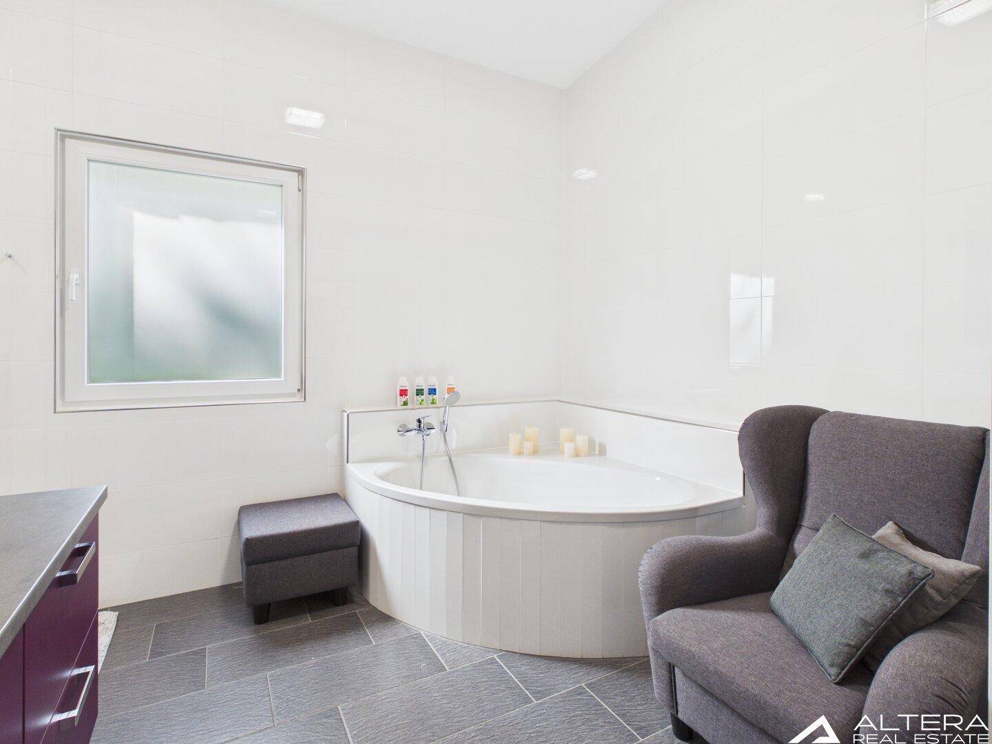 Geräumiges Badezimmer mit Eckbadewanne, Sessel und großem Fenster.
