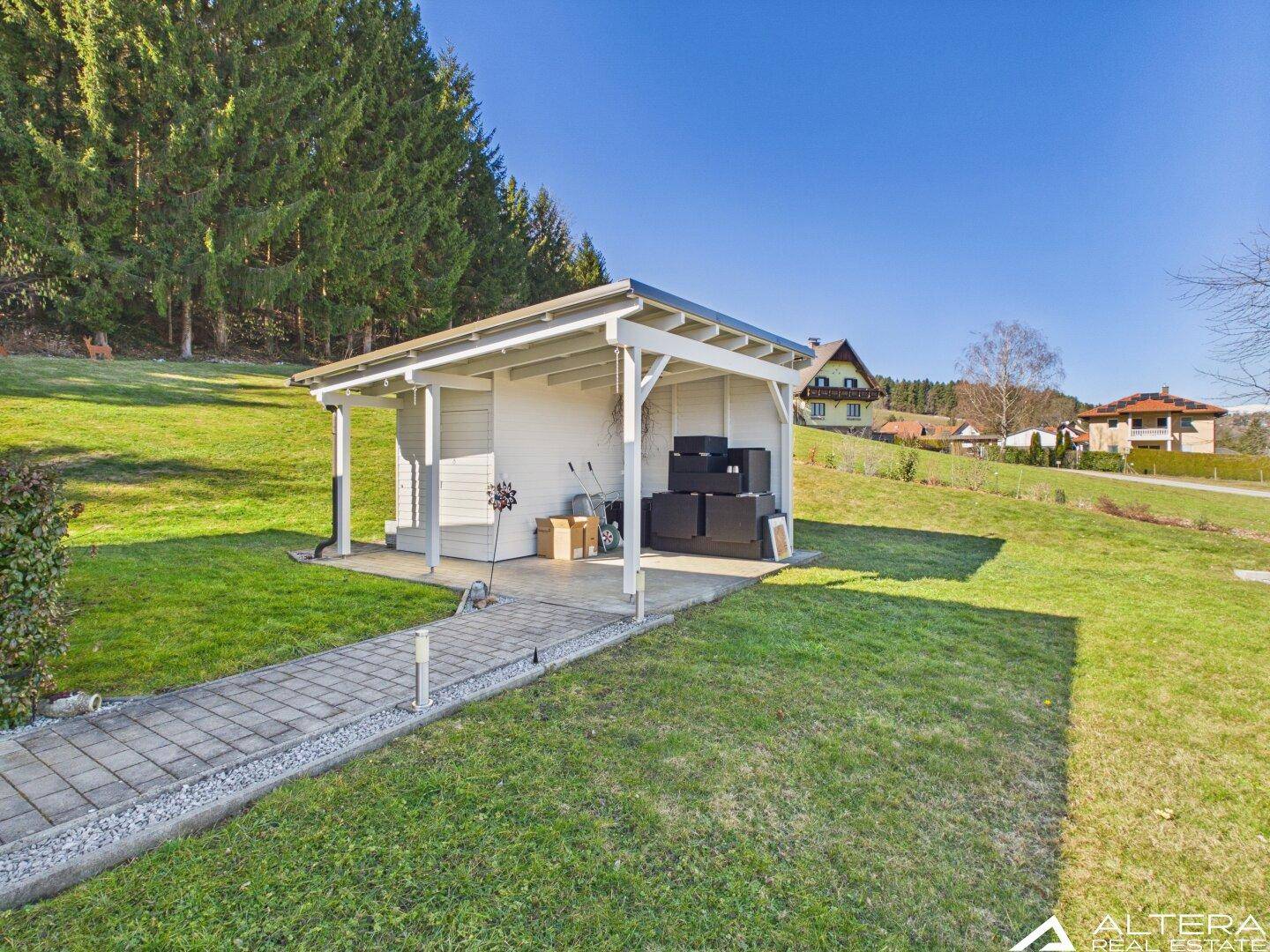 Kleines Nebengebäude mit überdachtem Bereich und Blick auf den Wald.