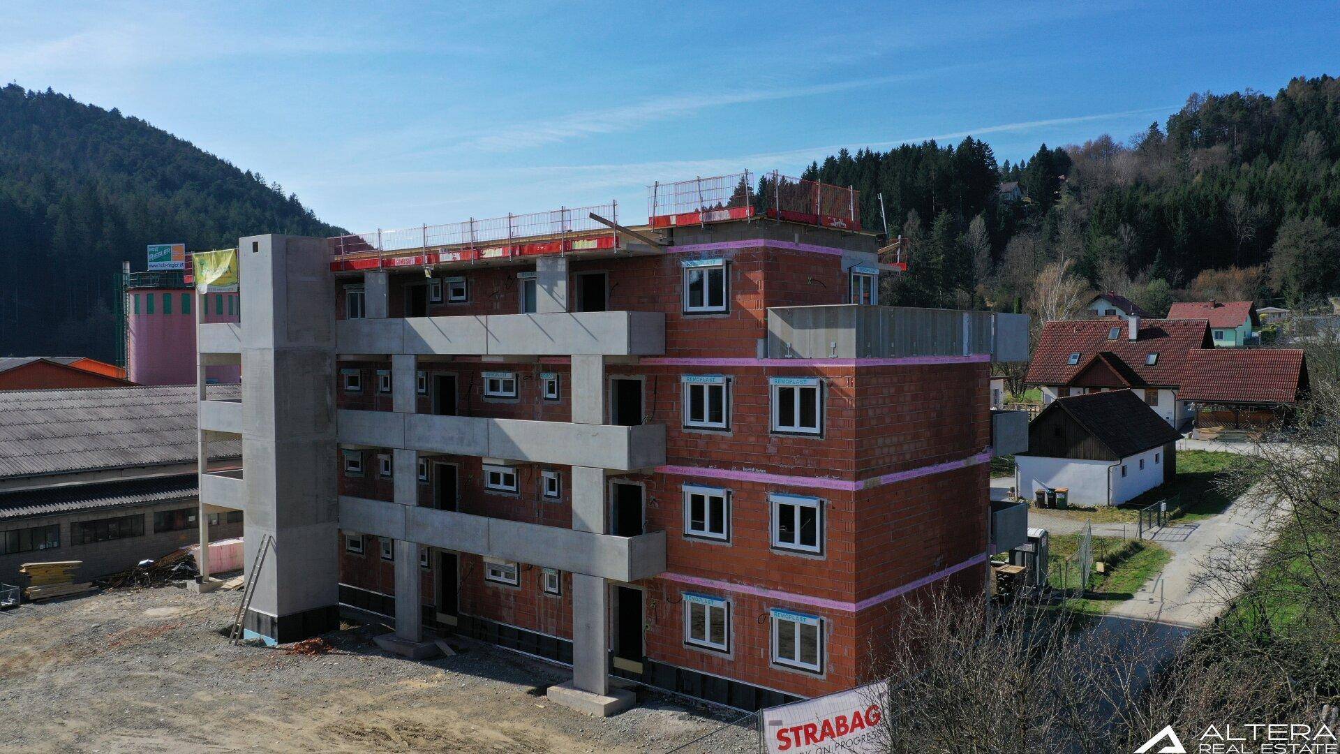 Neubau im Rohbau mit Fenstern und Blick auf bewaldete Hügel und umliegende Häuser.