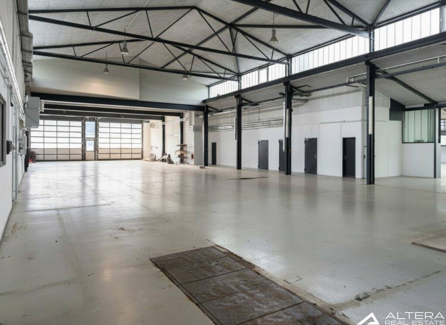 Helle Industriehalle mit Rolltoren, hohen Decken und robustem Betonboden, geeignet für verschiedene gewerbliche Nutzungen.
