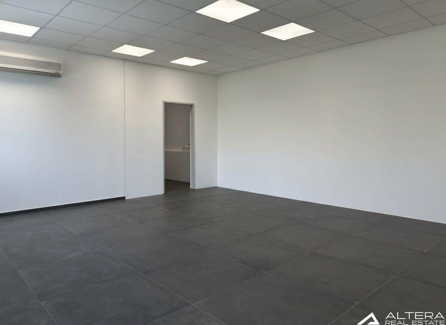 Leerer Büroraum mit Klimaanlage, dunklem Fliesenboden und Zugang zu einem Nebenraum.