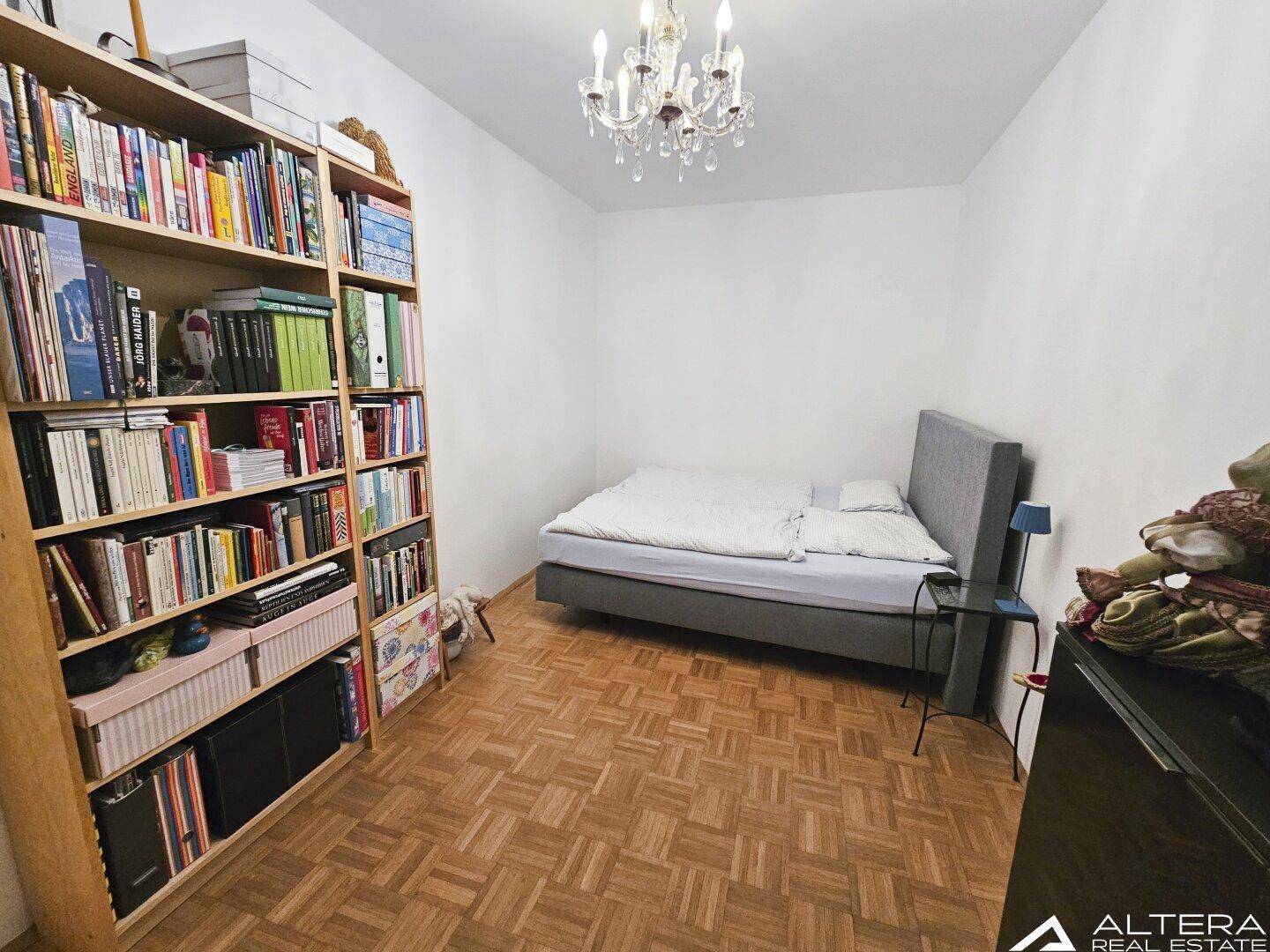 Gemütliches Schlafzimmer mit Parkettboden, Bett und einem dekorativen Kronleuchter.
